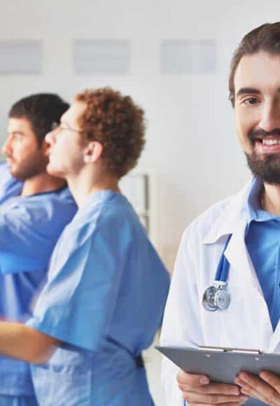 Friendly doctor Portrait of friendly doctor looking at camera on background of his colleagues interacting